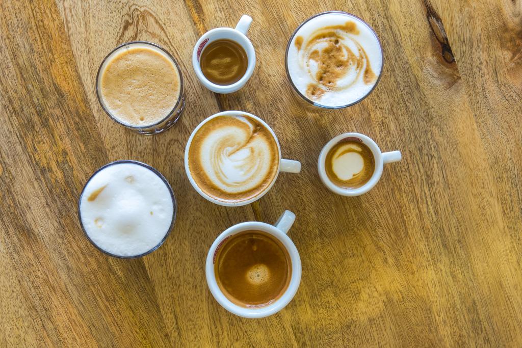 Verschiedene Arten von Kaffee in Tassen auf Holztisch, Ansicht von oben