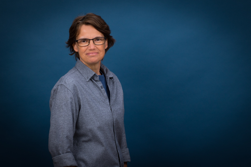 Bewerbungsfoto Headshot Porträt einer Frau-mit Brille vor blauem Hintergrund